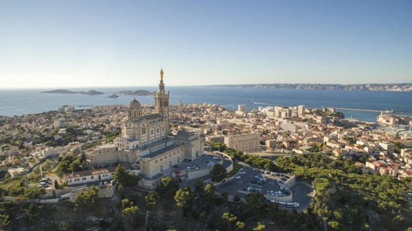 Høydevinkelsikt av bybildet ved sjøen. Notre Dame de la Garde i Marseille mot klar himmel. Bygninger ved sjølandskap på solrik dag.