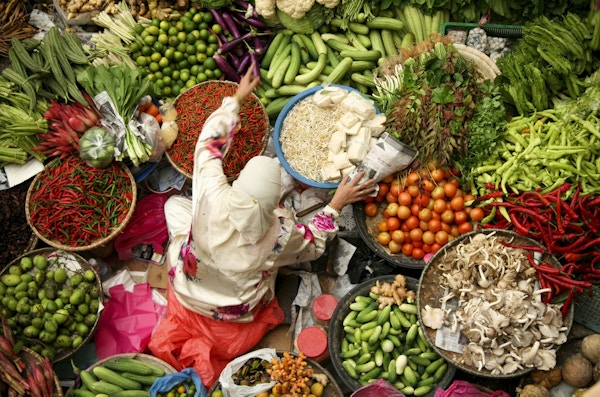 Muslimsk kvinne som selger friske grønnsaker på markedet i Malaysia