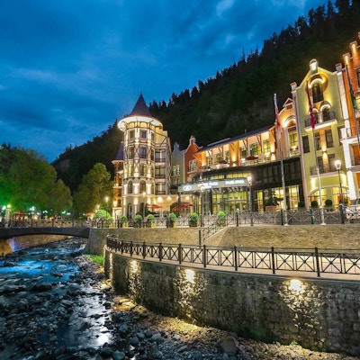 Kveldsbilde med hotell Crowne Plaza som er opplyst og ligger ved vannet med skogen i bakgrunnen