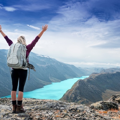 Ung turistkvinne som føler seg fri og står med hendene i været på toppen av fjellstien mens hun ser på et vakkert landskap