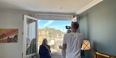 En mann filmer ut av et vindu med en person foran og utsikt over en storby
