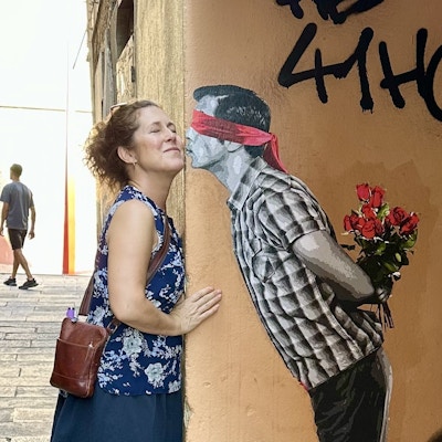 En dame står ved en vegg med et maleri av en mann som kysser