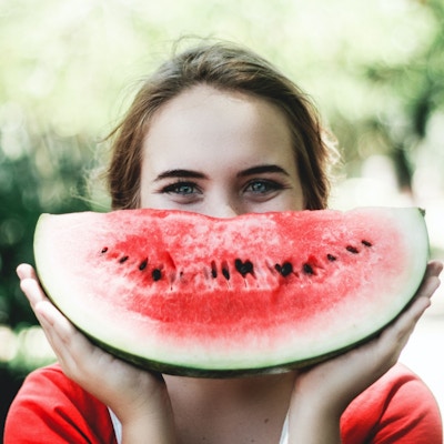 Kvinne som har et stykke vannmelon foran ansiktet