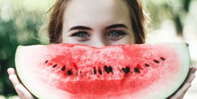 Kvinne som har et stykke vannmelon foran ansiktet
