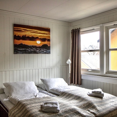 Innsiden av et rom med dobbeltseng, vindu og kunst på panelveggen over senga