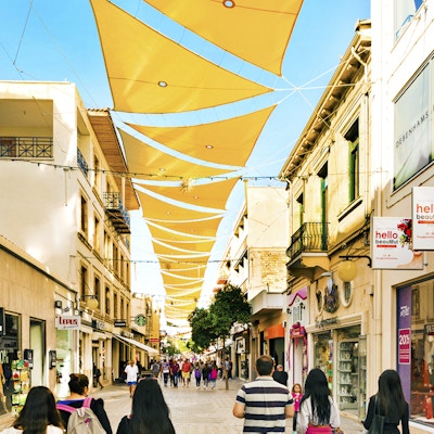 Personer går i en handlegate med et gult seil over som gir skygge