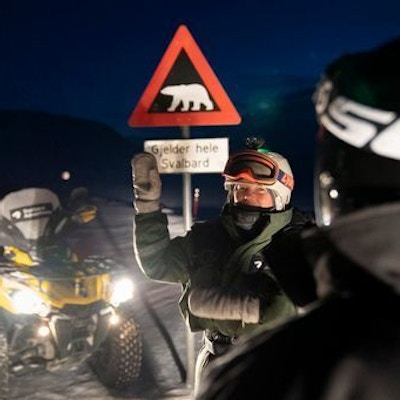 Gul ATV ved siden av fareskilt for isbjørn og vinkende mann med varme klær og hjelm