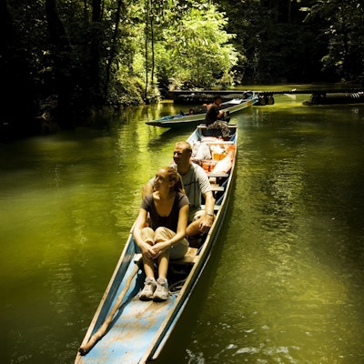 To personer i en lang smal båt på en elv