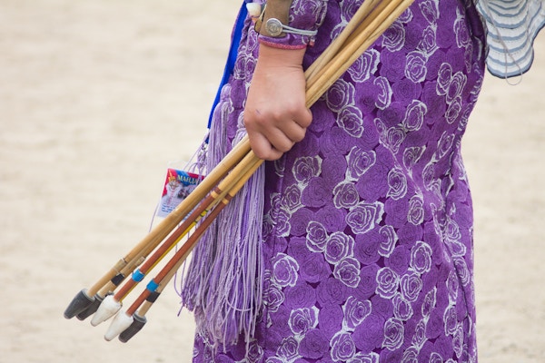 Nærbilde tatt av en mongolsk kvinnelig bueskytter som bærer tradisjonelle klær med vakkert lilla mønster mens hun holder pilene klare til spillene.