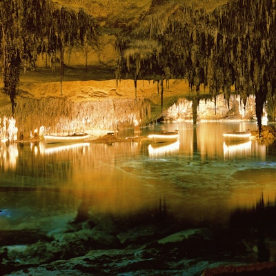 Innsiden av en grotte med lyssetting, vann, opplyste båter og dryppstein i taket