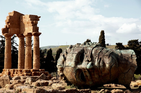 Bronsehode av en kolossistatue foran Castor og Pollux gamle greske tempelruiner på det arkeologiske stedet for templedalen som ligger på Agrigento, Sicilia. Italia.