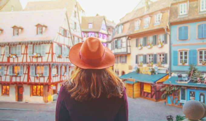 Ung glad kvinne som gleder seg over julen i gamlebyen opplyst og dekorerer magisk som en eventyr i Noels festlige sesong i Colmar, Alsace, Frankrike