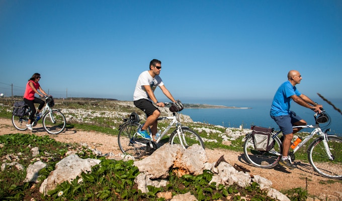 Tre personer sykler på grussti langs kysten i Puglia