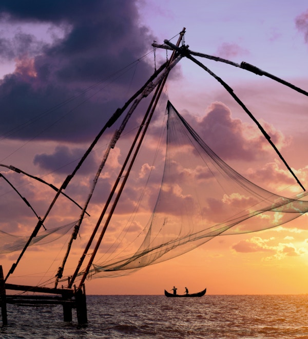 Solnedgang over kinesiske fiskenett og båt i Cochin (Kochi), Kerala, India.