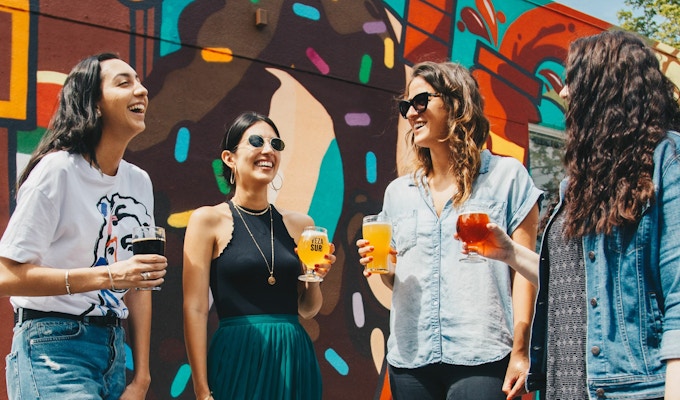En gruppe jenter står og ler sammen med et glass i hånda