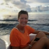 Dame i oransje t-skjorte sitter i båt i solnedgang på havet