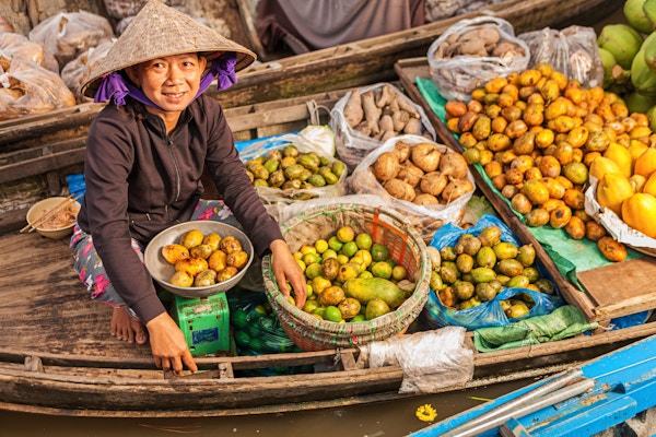 Vietnamesisk, kvinnelig fruktselger på flytende marked, som selger frukt fra båten sin i Mekong-elvedeltaet, Vietnam.
