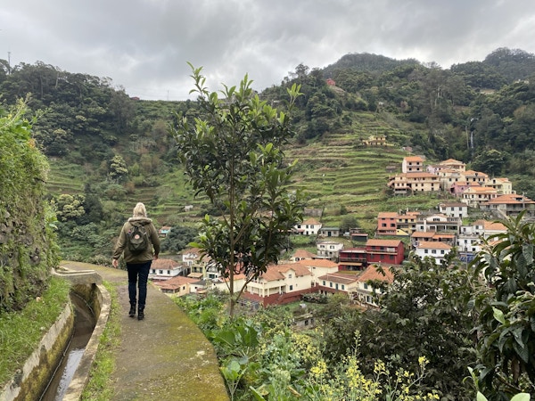 En dame går på levadastien blant hus og grønne, frodige fjell på Madeira