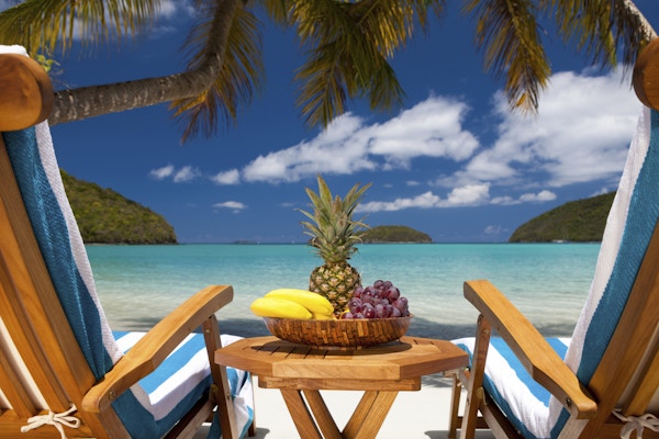 to hvilestoler med teak og et bord fullt av eksotisk frukt på et tropisk karibisk badeby