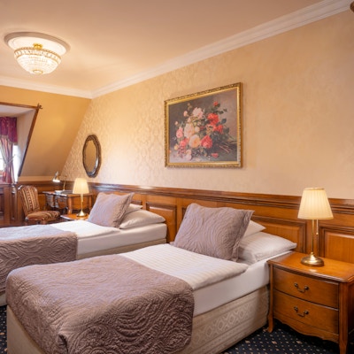 Hotellrom med to senger, teppe på gulvet og gamle, flotte møbler