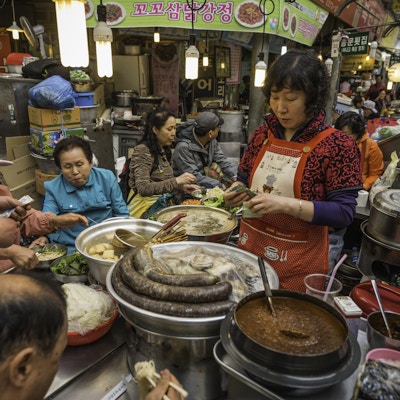 Seoul, Korea - 29. april 2013: Lokale mennesker sitter og spiser nudler og tradisjonell koreansk mat på en fullsatt gatematkjøkken som serveres av en kvinnelig handelsmann i det pulserende og livlige Dongdaemun-markedet i hjertet av Seoul sentrum.