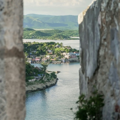 Utsikt mot fjell, hav og hus fra en glippe i festningsmuren ved el Morro, Santiago de Cuba